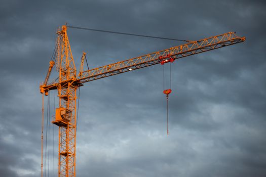 High tower crane for building city skyscraper structure construction over cloudy sky sunset