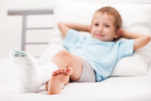 Human healthcare and medicine concept - little child boy with plaster bandage on leg heel fracture or broken foot bone