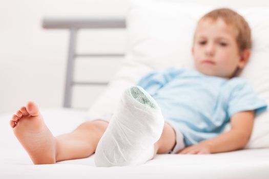 Human healthcare and medicine concept - little child boy with plaster bandage on leg heel fracture or broken foot bone