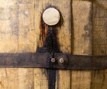 Macro close up shot of the wooden bung or cork in a barrel of oak used for holding bourbon whisky. The contents are leaking down the side of the barrel over the hoop