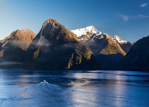 Sailing into Milford Sound on South Island of New Zealand in early morning as the sun rises above the mountains