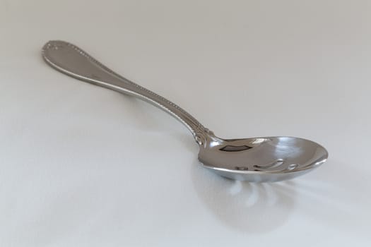 Decorated slotted serving or dessert spoon for draining wet vegetables in side view on fine white tablecloth with pattern just visible
