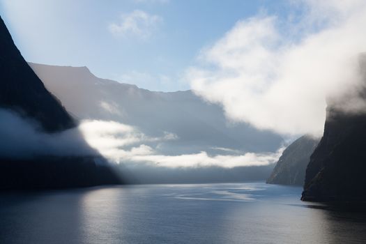Sailing into Milford Sound on South Island of New Zealand in early morning as the sun rises above the mountains