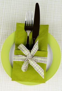 Elegant Table Setting with Fork and Table Knife into Green Napkin Decorated with Checkered Bow on Plate. Top View