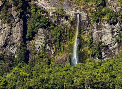 Waterfall on side of Milford Sound on South Island of New Zealand in early morning as the sun rises above the mountains