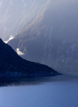 Sailing into Milford Sound on South Island of New Zealand in early morning as the sun rises above the mountains