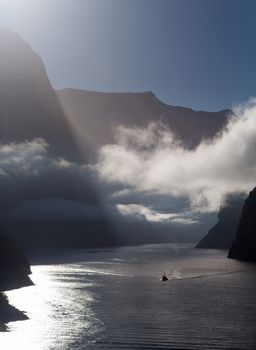 Sailing into Milford Sound on South Island of New Zealand in early morning as the sun rises above the mountains