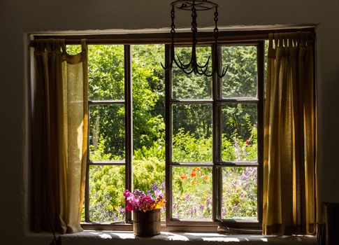 View of cottage garden behind a traditional English garden in summer with small brick cottage home and flowering plants and flowers