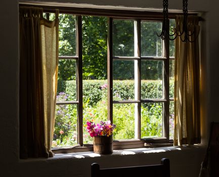View of cottage garden behind a traditional English garden in summer with small brick cottage home and flowering plants and flowers