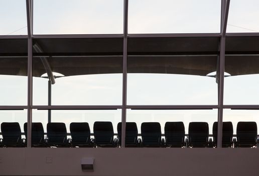 Silhouettes of deck or beach recliner chairs in a line under a sun shade on deck of cruise ship on a grey cloudy day