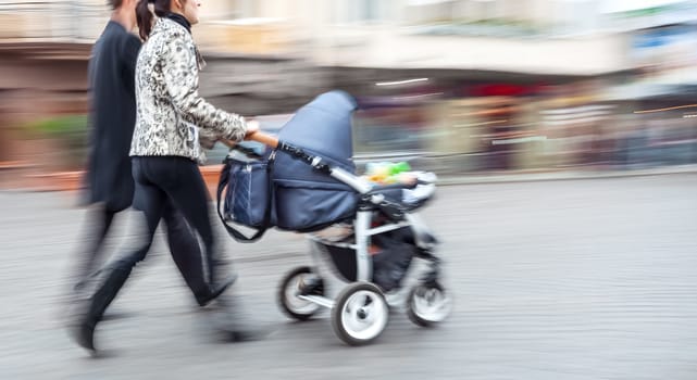 Young family with small children and a pram walking down the street. Intentional motion blur