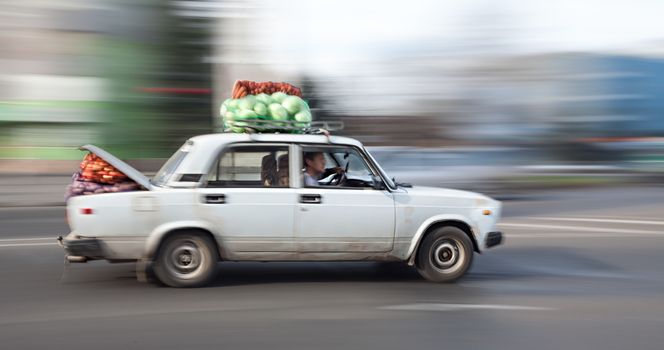 Old car loaded with cabbage and carrots rides through the city streets. Intentional motion blur