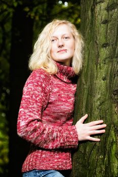 Beautiful young blond woman daydreaming at night standing outdoors against a tree, she is illuminated