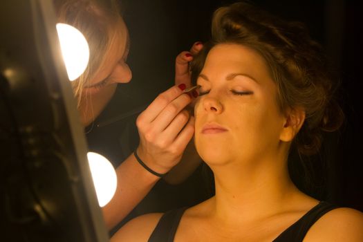 Woman applying make up for a bride in her wedding day near mirror, wamr light from lightbulbs