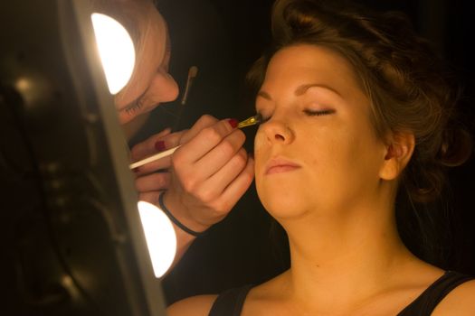 Woman applying make up for a bride in her wedding day near mirror, wamr light from lightbulbs
