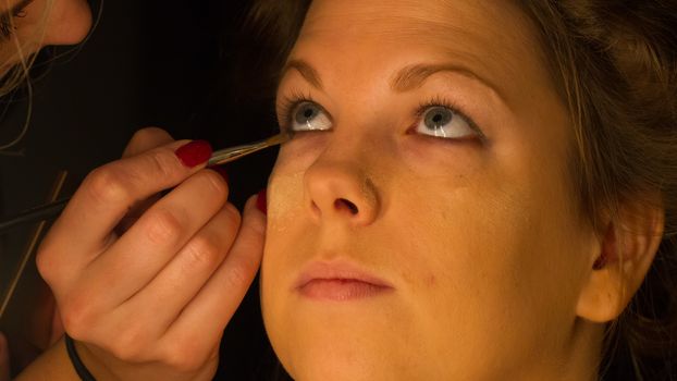 Woman applying make up for a bride in her wedding day near mirror, wamr light from lightbulbs