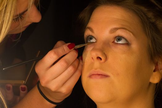 Woman applying make up for a bride in her wedding day near mirror, wamr light from lightbulbs