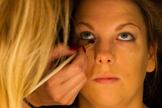 Woman applying make up for a bride in her wedding day near mirror, wamr light from lightbulbs