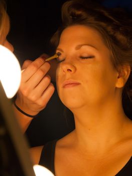 Woman applying make up for a bride in her wedding day near mirror, wamr light from lightbulbs