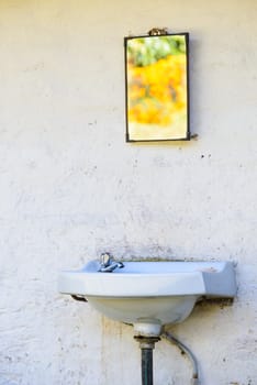 Outdoor sink on a white wall, mirror reflecting bright orange flowers