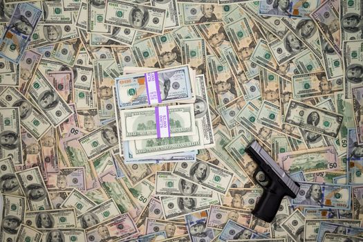 Conceptual image of the monetary proceeds of criminality with a handgun lying on a background of 100 dollar American bills alongside a pile of cash