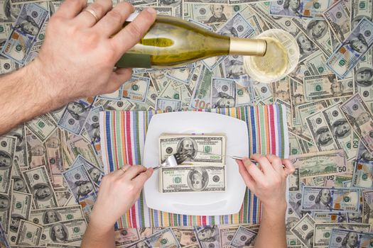 Man eating dollar bills as a servant pours champagne from a bottle overhead on a background of money in a conceptual image of wealth and extravagance