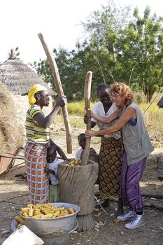 a French tourist participates in folding corn in good spirits with women from a village in Burkina Faso