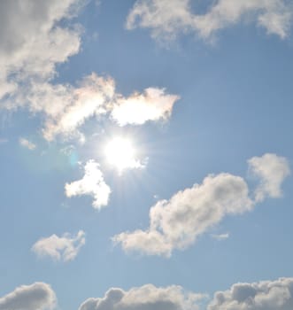 Soft clouds on blue sky background with shiny sun in the center
