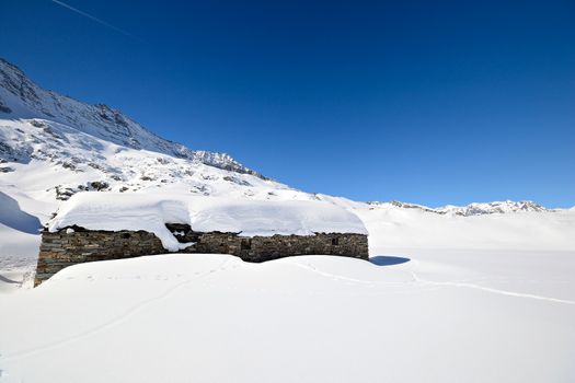 Winter landscape in the italian Alps with abandoned pasture hut covered by snow. Back country ski tracks.