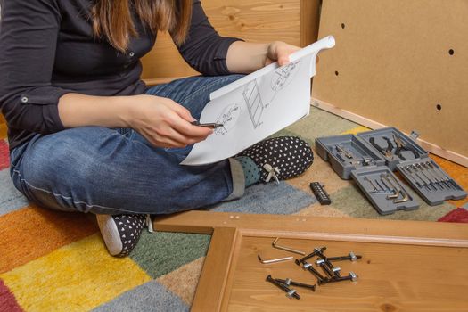 Closeup of girl with tools reading the instructions to assemble a new furniture for home
