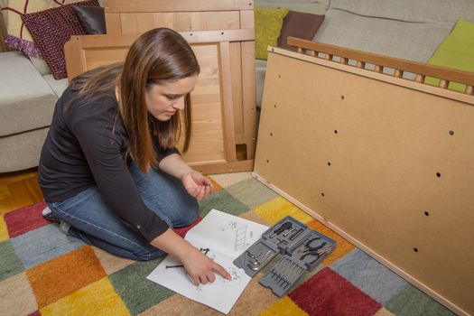 Concentrated girl with tools reading the instructions to assemble a new furniture for home