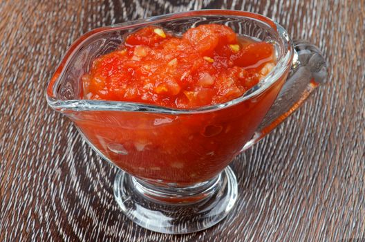 Hot Salsa Sauce in in Glass Gravy Boat isolated on Wooden background