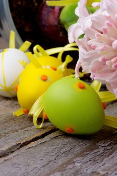Multi Colored Easter Eggs Pink Hyacinth with Yellow Ribbons closeup on Rustic Wooden background