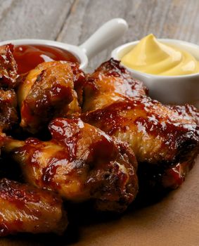 Hot Chicken Legs and Wings Barbecue with Ketchup and Cheese Sauces on Wooden Plate closeup