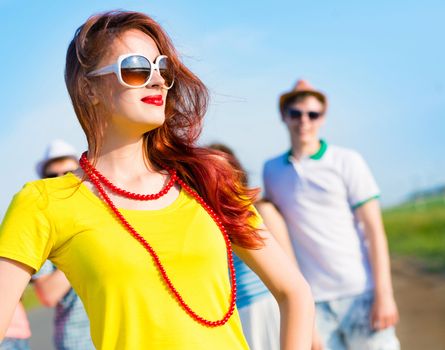 stylish young woman in sunglasses on the background of blue sky and friends