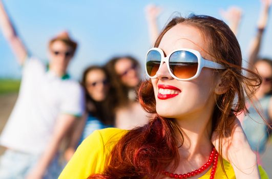 stylish young woman in sunglasses on the background of blue sky and friends