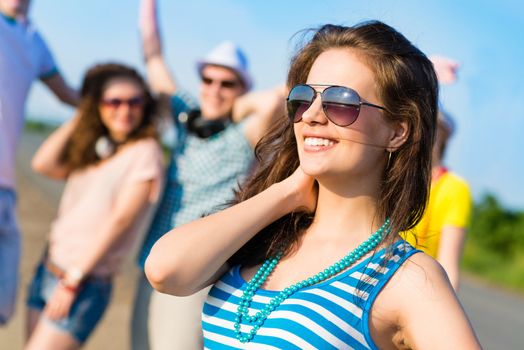 stylish young woman in sunglasses on the background of blue sky and friends