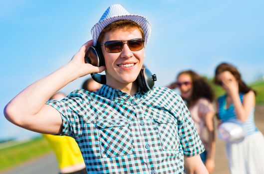 young man in sunglasses, headphones holds a hand on a background of blue sky and friends