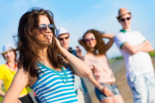 stylish young woman in sunglasses on the background of blue sky and friends