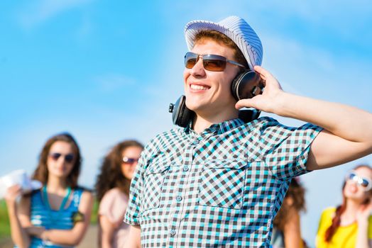 young man in sunglasses, headphones holds a hand on a background of blue sky and friends