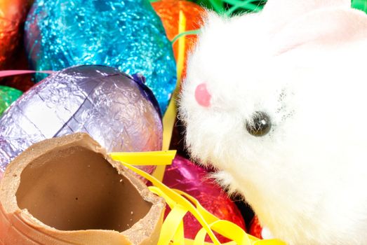 Close-up of a bunny toy eating a chocolate egg on an easter nest.