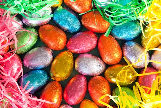 Close-up of pile of colorful chocolate Easter Eggs surrounded by colorful grasses.