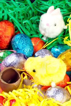 Close-up of a fluffy yellow chick racing a fluffy white bunny over a pile of colorful eggs and grasses to a chocolate egg.