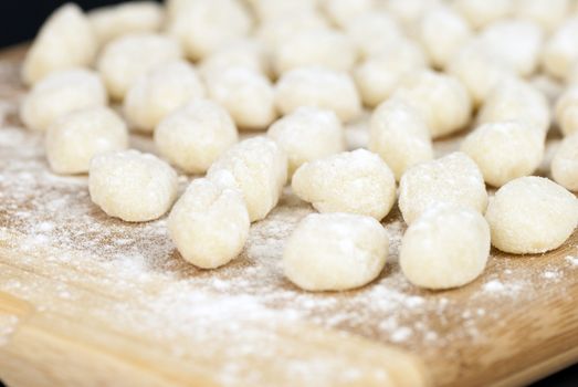 Close-up of a chef displaying freshly prepared gnocchi on a bamboo cutting board.