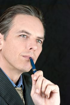 Close-up of a businessman thinking while tapping his pen to mouth.