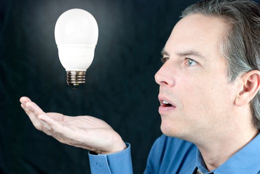 Close-up of a businessman looking awestruck at a glowing light bulb floating above his hand.