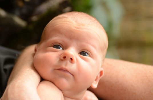 newborn baby with bright eyes held by mother