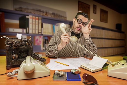 Employee with glasses talking on the phone and making jokes with the hand in the office in the 1960s