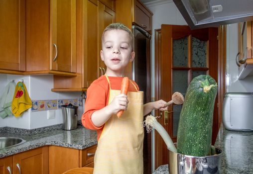 Cute child chef with apron cooking big zucchini and other vegetables in a pot on the kitchen