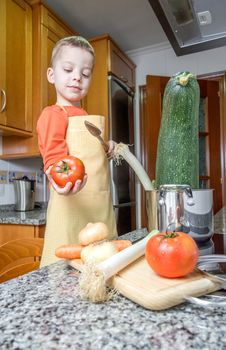 Cute child chef with apron cooking big zucchini and other vegetables in a pot on the kitchen